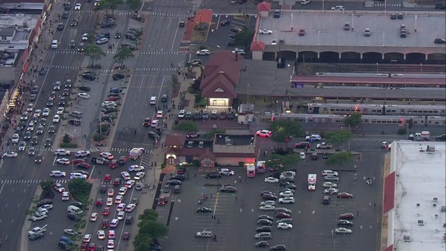 An aerial view of the LIRR Long Beach station on Long Island. A number of police vehicles and several ambulances are parked in parking lots and on nearby streets. 