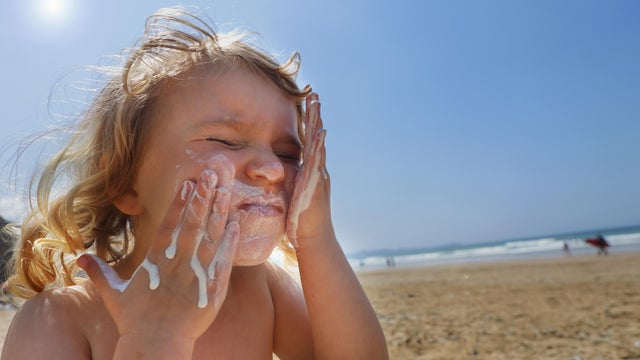 Toddler girl applying suncream 